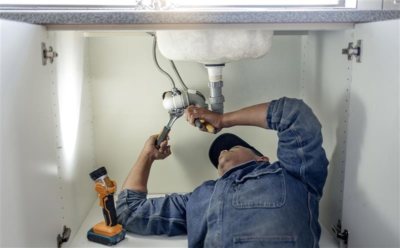 Plumber repairing pipes beneath a bathroom sink in Suwanee