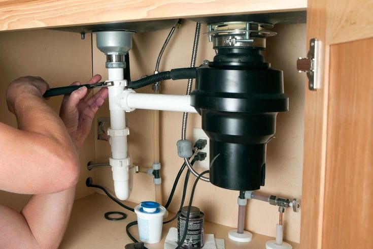 Plumber installing a garbage disposal beneath a kitchen sink in Suwanee
