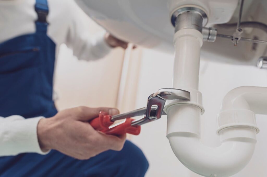 Plumber repairing a white drain pipe beneath a sink in Suwanee