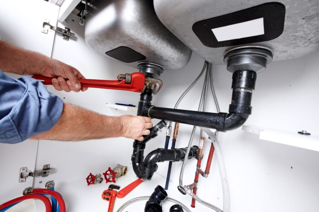 Plumber repairing drain pipes beneath a kitchen sink in Suwanee